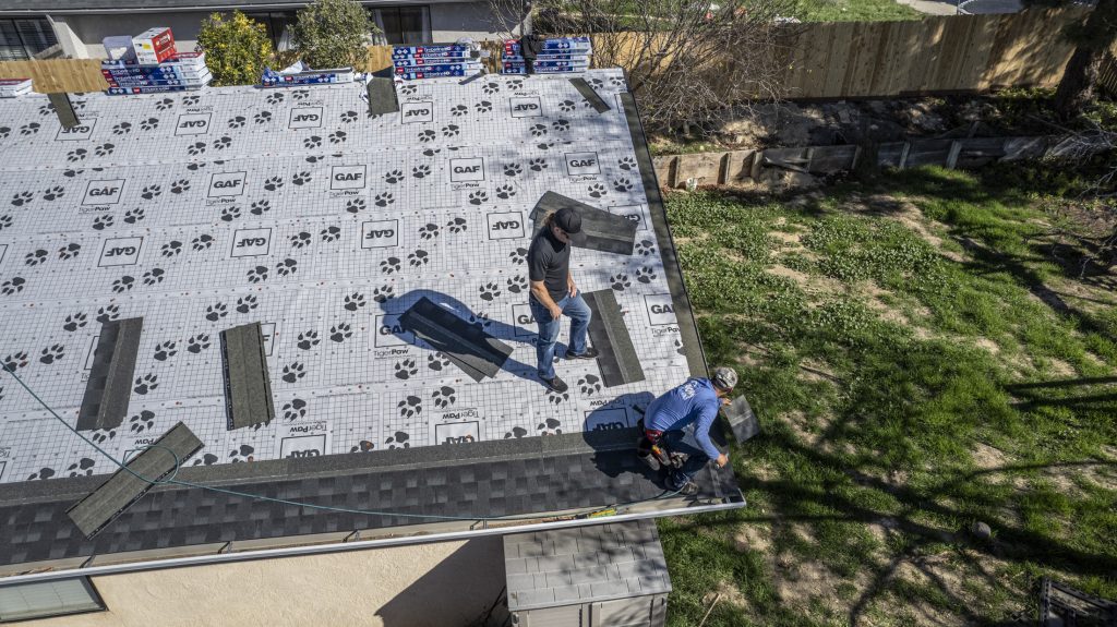 Axiom contractors laying down new asphalt roofing, showing what is included in a roof replacement